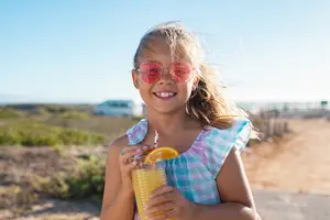 A smiling young girl holding a glass of orange juice with a straw and an orange slice on the rim