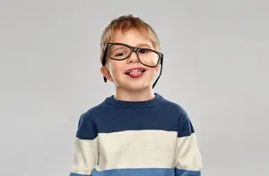 A young boy wearing glasses and a blue and white striped sweater, sticking his tongue out