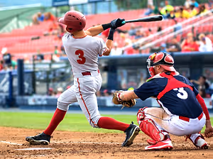 A baseball player wearing a number 3 jersey swings his bat while the catcher crouches behind him, both wearing helmets and gloves, on a baseball field with spectators in the background.