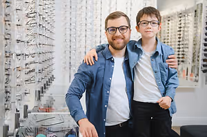 A man and a young boy wearing glasses standing in a store that sells glasses