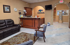 An interior of a waiting room with a leather couch, chairs, and a desk with a monitor.