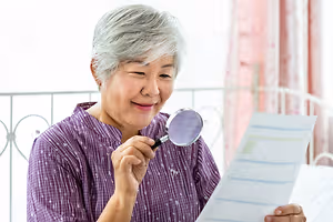 An older woman holding a magnifying glass and reading a document