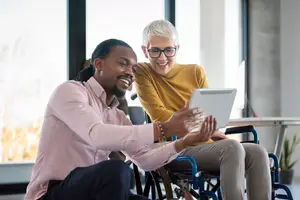 A man and woman sit together on a chair and look at a tablet