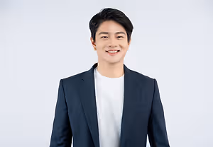 A smiling man in a white t-shirt and a navy blue blazer standing against a white background