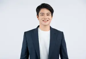 A smiling man in a white t-shirt and a navy blue blazer standing against a white background