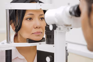 A woman with brown eyes is looking into a device while a man is looking at her through a microscope.