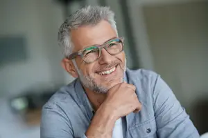 A man wearing glasses and a blue shirt smiles and poses for a photo