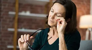 A woman in a green top is adjusting her glasses and closing her eyes.