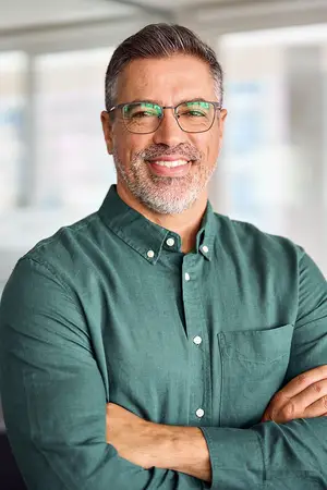 A smiling man in a green shirt stands with his arms crossed in an office.