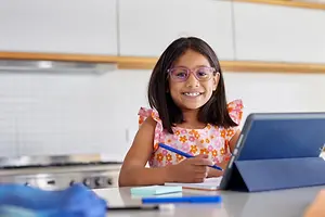 Smiling girl wearing purple glasses doing homework at a table