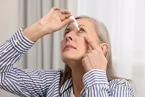 Older woman applying eye drops to her eye