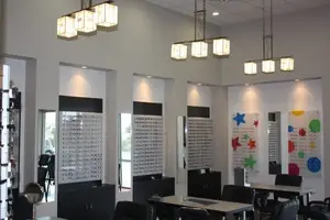 Interior of an optical shop with tables, chairs, mirrors, and hanging lamps.