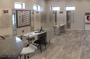 A room with furniture and a poster on the wall. The room has chairs, desks, a mirror, and a poster with a picture of a woman.