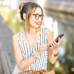 A woman in a striped dress and glasses is looking at her phone on a sunny day.