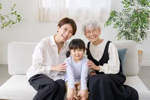 Three people are sitting on a couch and smiling for a picture, with two women wearing glasses and a child sitting between them.
