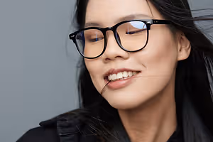 Portrait of a smiling woman wearing black glasses and a black jacket against a gray background