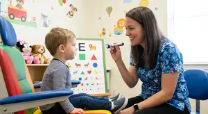 a woman holds a flashlight near a young boy's face in a pediatric dentist's office