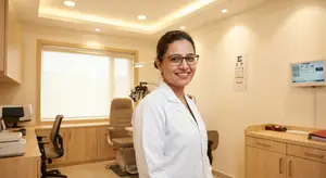 A woman in a lab coat stands in a doctor's office and smiles at the camera