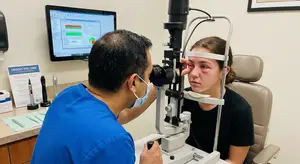 An eye doctor is examining a patient's eye with a slit lamp in a medical clinic.