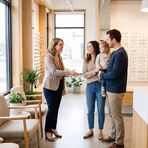 A family of four stands in front of a desk and speaks to a woman in a tan blazer in a medical office.