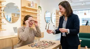 A woman with glasses on her face is looking at frames with a smiling woman next to her in an optical shop