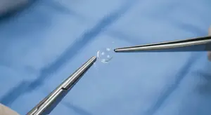 A pair of scissors is cutting a transparent piece of plastic on a blue cloth.
