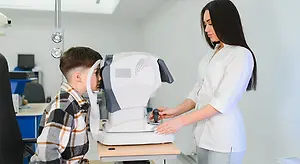 A young boy is having his eyes examined by an optometrist in a medical office.