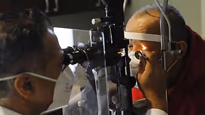 An elderly man wearing a face mask having his eye examined by an eye doctor