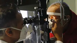 An elderly man wearing a face mask having his eye examined by an eye doctor