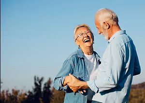 Happy older couple dancing in an outdoor field with a clear blue sky in the background