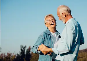 Happy older couple dancing in an outdoor field with a clear blue sky in the background