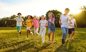 A group of children run through a grassy field as the sun sets behind them, smiling and laughing