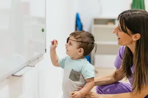 A mother with a young boy who has an eye patch is pointing at a whiteboard.
