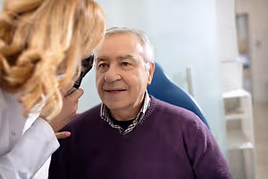 A woman doctor is checking the ears of a patient in a medical room with a stethoscope