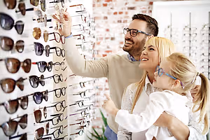 A man and woman are smiling while looking at glasses in a shop with a little girl standing between them