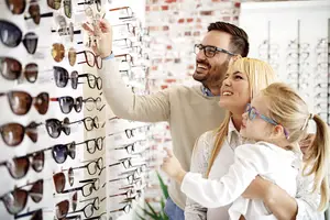 A man and woman are smiling while looking at glasses in a shop with a little girl standing between them