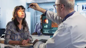 An elderly woman sits in front of a monitor while a doctor points at an image on the screen