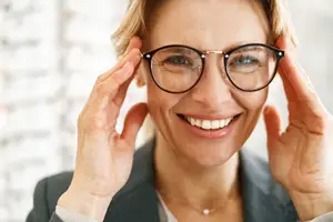 A woman wearing glasses and smiling while adjusting them with her hands