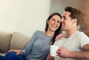 A man and a woman sitting on a couch while holding a cup and smiling at each other
