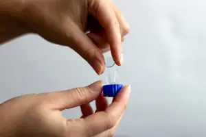 A person is placing a blue container with a clear object inside on a white surface.