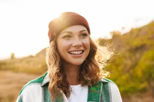 Portrait of a smiling woman standing in a field wearing a white t-shirt and a green plaid jacket and a brown beanie hat