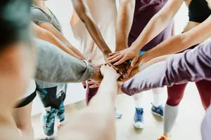 A group of people are gathered together and are putting their hands together in a circle.