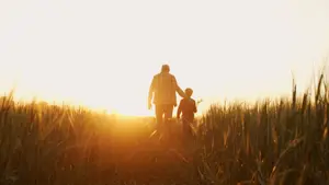 Two people are walking in a tall grass field during the sunset.