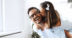 A man and a young girl smiling and hugging each other inside a house