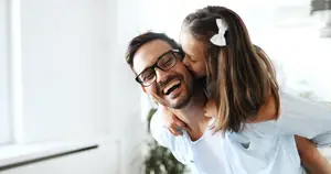 A man and a young girl smiling and hugging each other inside a house