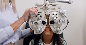 A woman is adjusting an eye-testing machine on a girl's head