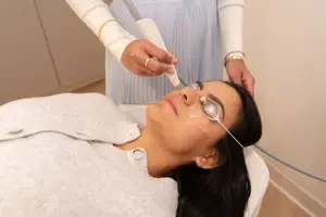 Eye care professional performing IPL therapy on patient around eyes 