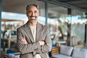 Smiling man in a beige suit with arms crossed in a modern office setting.