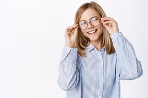A young girl with blonde hair wearing a blue checkered long-sleeve shirt and glasses, smiling and posing for a photo.