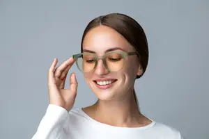 A woman wearing glasses is smiling and looking at the camera with a hand on her face.